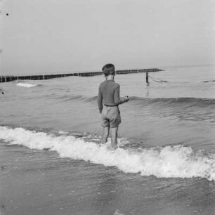 Kind der Gremmlers steht im Wasser der auflaufenden Wellen am Strand von Henkenhagen (heute: Ustronie Morskie)
