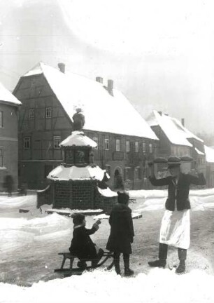 Kinder mit Schlitten und Stollenträger am Töpferbrunnen (1928; K. Feuerriegel), im Hintergrund Bäckerei Otto Weise