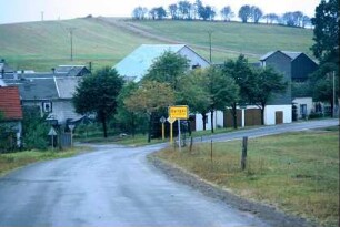 Straße mit Ortsschild und ersten Häusern