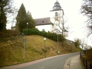 Ansicht von Norden mit Kirche (im Kern Romanisch-Kirchturm 14 Jh) über Kirchhofmauer (Wehrgang im 18 Jh abgetragen) in erhöhter Lage über dem Ort