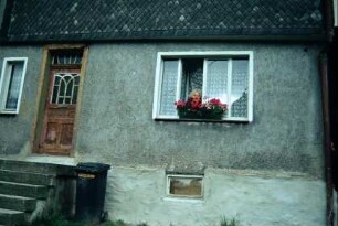 kleines Haus mit Treppenaufgang, alter Holztür, Frau am Fenster