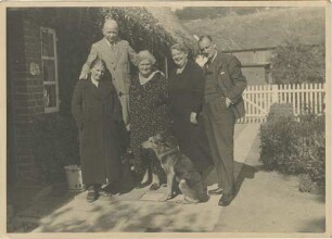 Kuöhl, Richard und Gertrud Emma Klara Kuöhl, geb. Suckau: Gruppenfoto: gemeinsam mit zwei Frauen, einem Mann, davor Schäferhund: Rohlfshagen, Kupfermühle: Schäferkate, vor Traufseite, links Eingangstür: Plattenweg, hinten Zaun, Gartentor, dahinter Atelier, Schuppen: im Hintergrund Wiese an Abhang