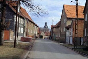 Straße mit anliegenden Häusern und Gehöften, hinten Kirche