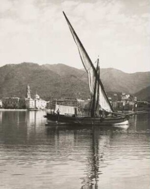 Rapallo. Italien. Segelschiff mit gerefften Segel im Hafen. Im Hintergrund die Silhouette der Stadt