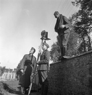 Hans-Adalbert von Stockhausen (links), Carl Albiker (Mitte) und Franz Prinz zu Sayn-Wittgenstein (auf der Friedhofsmauer) bei Außenaufnahmen einer Kirche (Aufnahme im Rahmen der Fotokampagne im besetzten Frankreich)