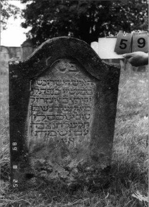 Grabstein 59 (Index: 100108157) Material: heller Sandstein Zustand: verwittert, versalzen Maße HxBxT: 89x58x10 cm Beschreibung: Stele mit geschwungenem eingezogenem Rundbogenabschluß, Schriftfeld eingetieft: Grabstein 59