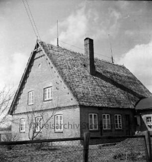 Bauernhaus mit Reetdach: davor Zaun und Garten: rechts Misthaufen