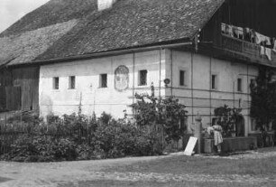Wohnhaus : Wohnhaus in den Alpen. Eine Frau trinkt aus einem davor liegendem Brunnen.