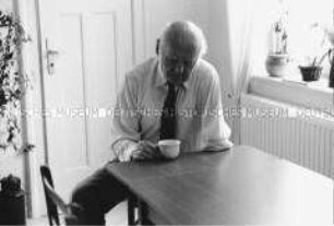 Älterer Mann sitzt mit einer Kaffeetasse an einem Ausziehtisch (Altersgruppe 14-17)