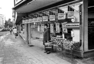 Wartender Mann mit Leineweber-Eainkaufstasche, Regenschirmen und Hut. Innenstadt Bielefeld