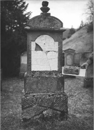 Grabstein 334 (Index: 100009390) Zustand: Vorderseite: Inschrifttafel mehrfach zerbrochen und wiedereingesetzt, kleine Teile fehlen Maße HxBxT: 188x60x20 cm: Grabstein 334