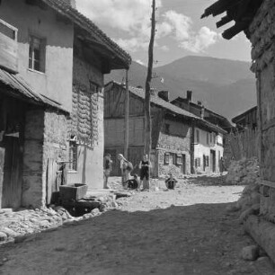 Alltagsbild. Frauen unterwegs in Bansko. Gestelle für das Trocknen der Tabakblätter am Wohnhaus und ein öffentlicher Brunnen in Bansko