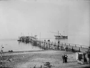 Blick vom Ostseestrand zu einer Seebrücke mit abfahrendem Dampfer