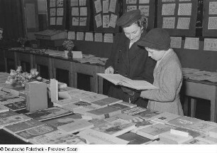 Ausstellungsbesucher an einem Bücherstand ein Buch lesend