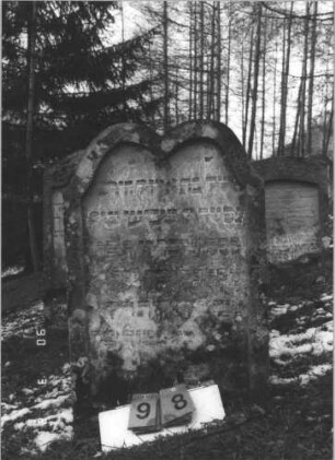 Grabstein 98 (Index: 99608782) Material: Sandstein Zustand: stärker verwittert Maße HxBxT: 91x58x13 cm Beschreibung: Stele mit geschwungenem Doppelbogen, vertiefter Textteil in gleicher Form: Grabstein 98