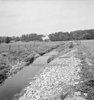 Beste: Flussregulierung: Zusammenfluss von Norderbeste und Süderbeste bei Blumendorf: Böschungserneuerung mit Bohlenwänden und Ziegelbrocken: vorn rechts und links befestigte Böschung: dahinter verkrauteter Flusslauf: hinten rechts sitzender Mann im Gras: im Hintergrund Herrenhaus Blumendorf und Park