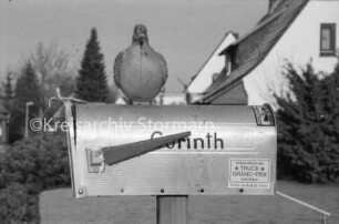 Briefkasten mit Taubenplastik, Anzeiger, Aufkleber und Namenszug "Corinth": hinten Vorgarten: rechts Einfamilienhäuser