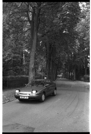Vorstellung des Mazda 323 Fließheck GLX, mit Klappscheinwerfern: auf Straße, hinten Alleebäume