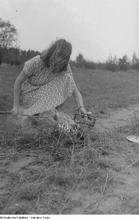 Renate Rössing setzt einen Kochtopf auf ein Feuer im Freien