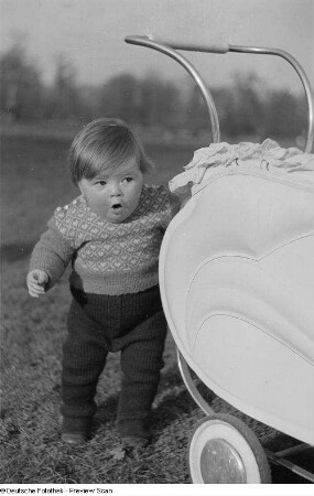 Kleines Kind, sich an einem Kinderwagen festhaltend