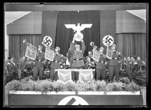 Musikkapelle mit vier Fanfarenspieler und Dirigent (im Hintergrund Reichsadler)