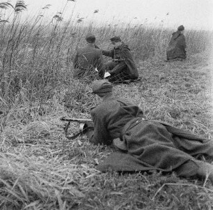 Deutsche Demokratische Republik. Grenze zwischen BRD und DDR. Offizier und Grenzpolizist bei einer Lagebesprechung mit Karte im Gelände, abseits zwei Grenzposten zur Sicherung des Abschnittes