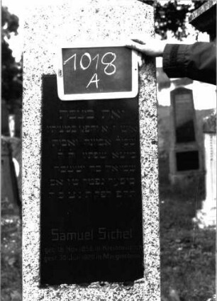 Grabstein 1018 (Index: 100104000) Material: Granit Zustand: gut erhalten Maße HxBxT: 178x47x20 cm Beschreibung: obeliskenartige Stele auf getrepptem Sockel, eingelassene hochrechteckige Schrifttafel: Grabstein 1018A