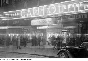 Menschen vor dem Kino Capitol in der Petersstraße mit Werbung für den Film "Keine Ferien für den lieben Gott" bei Nacht
