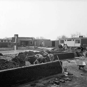Dörfergemeinschaftsschule: Neubau: Bauarbeiten am Fundament und den Grundmauern: hinten rechts Arbeiter: im Hintergrund Schulgebäude