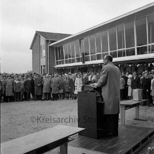 Am Exerzierplatz: Mittelschule (Gemeinschaftsschule) Harksheide: Einweihung: Bürgermeister Carl Lange hält eine Rede, dahinter Gäste vor dem neuen Schulgebäude