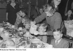 Kinder und Eltern an einer gedeckten und geschmückten Tafel bei der Weihnachtsfeier des Verlags Volk und Wissen