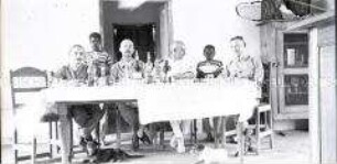 Vier Deutsche, davon drei in Uniform, an gedeckter Tafel mit afrikanischen Hausjungen
