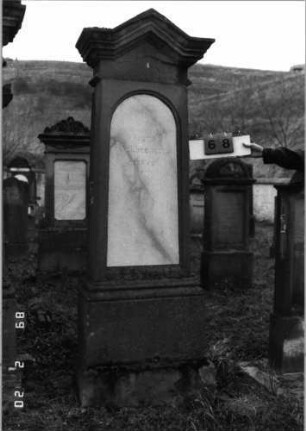 Grabstein 68 (Index: 99798582) Material: Sandstein, Schriftplatte Marmor Zustand: gut, Abschluß leicht beschädigt Maße HxBxT: 225x55x27 cm Beschreibung: Stele mit giebelartigem Abschluß, Schriftplatte mit Rundbogenabschluß, Sockel: Grabstein 68