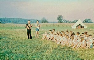 Kreisjugendheim: Gruppe von Kindern beim Singen auf der Wiese, dahinter Zeltlager