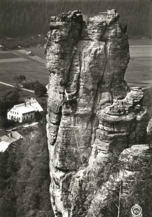 Böhmische Schweiz, Eiland (Ostrov). Wurzelstein (Kořenáč). Seilschaft Ehrhardt Renger in den Ausstiegsrissen des Alten Weges (IV). Blick zum Gasthaus Bergkeller