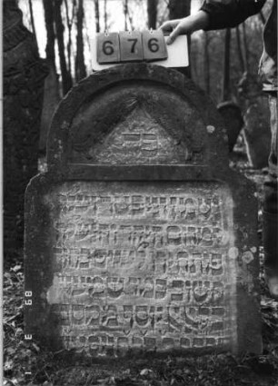 Grabstein 676 (Index: 99752407) Material: Sandstein Zustand: gut, Stele eingesunken Maße HxBxT: 102x77x17 cm Beschreibung: Stele, eingezogener Rundbogenabschluß, rechteckiges Schriftfeld eingetieft Symbolik: zwei Fische, die sich an den Mäulern berühren: Grabstein 676