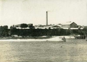 Fabrikanlage mit Industrieschornstein am Ufer eines Gewässers