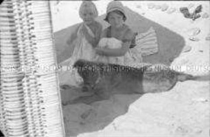 Zwei kleine Mädchen mit Hund am Strand von Köslin, hinter einem Strandkorb im Schatten sitzend