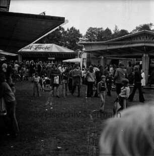 Frühjahrsmarkt: Volksfest: Exer: hinten rechts Karussell, hinten links Jahrmarktsbude: dazwischen Besucher: hinten Mitte Bäume
