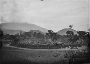 Siedlung : Blick von einer Anhöhe auf eine von Palisaden geschützte Siedlung.Im Hintergrund der Mount Meru von Wolken verhangen
