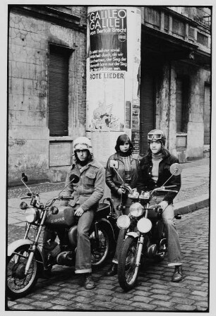 Jugendliche mit Motorrädern vor einer Litfaßsäule