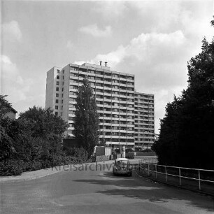 Königsberger Straße: fahrender Pkw, dahinter die Wohnhochhäuser der Straße Im Hölk (Siedlung Ehmkenberg II), Blick Richtung Südosten