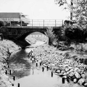 Norderbeste: vorn Böschung nach Besatz mit Feldsteinen: Holzpfähle im Wasser: hinten Brücke der Bundesstraße B 75: links darauf Lkw: rechts Büsche