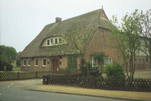 Wilstedt: Dorfring 7: traufständiges Bauernhaus mit Reetdach: Giebelseite ehemaliger Wirtschaftstrakt: rechts rechtwinkliger Anbau Stalltrakt mit Verbretterung an Obergeschoss: links Traufseite mit Eingangstür, breite Dachgaube: davor Hofeinfahrt