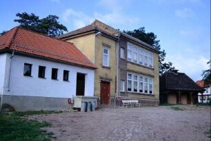 altes Schulgebäude mit neuem Sanitäranbau; dahinter Haus mit Arkadengang