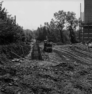 Sülzberg: links Baugrube:in der Mitte Bagger, Baumaterial, Gerätschaften und Erdhaufen: hinten rechts Hochhaus mit Gerüst im Bau: Bäume