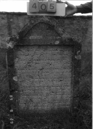 Grabstein 405 (Index: 100107902) Material: Kalkstein Zustand: verwittert, leicht eingesunken Maße HxBxT: 112x76x13 cm Beschreibung: Stele mit geschwungen eingezogenem Bogenabschluß, Schriftfeld rechteckig eingetieft: Grabstein 405