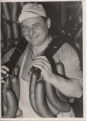 In einer Fleischwarenfabrik. Ein Fleischer trägt geräucherte Würste