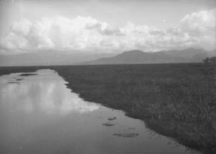 Senke von Toluca : Ebene Graslandschaft mit Gewässer. Im Hintergrund Berge