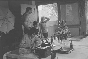 Höfgen. Akt-Pleinair 1979. Die Fotografen Eva Mahn, Günter Rössler und andere Teilnehmer im Gespräch, am Tisch sitzt ein Fotomodell mit Turban